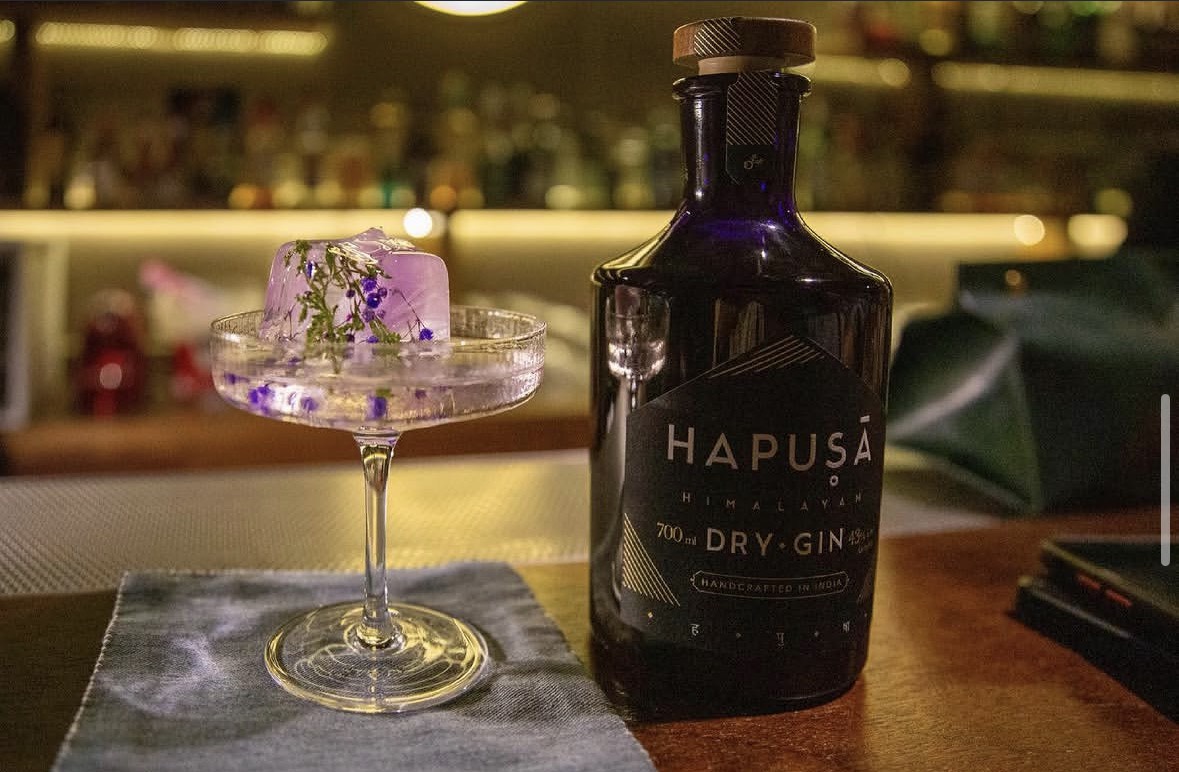 吧台上的一杯紫色琴酒調酒與 Hapusa 琴酒酒瓶